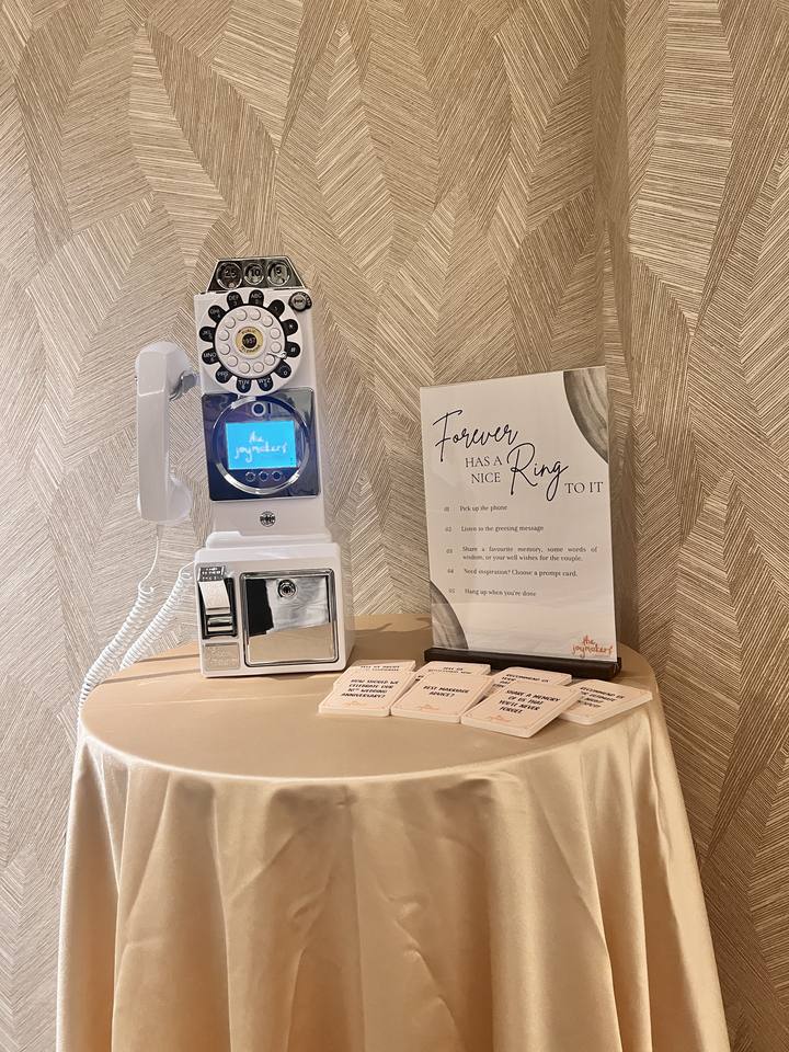 A white retro payphone guestbook on a round table with a champagne cloth, a wedding sign and message cards